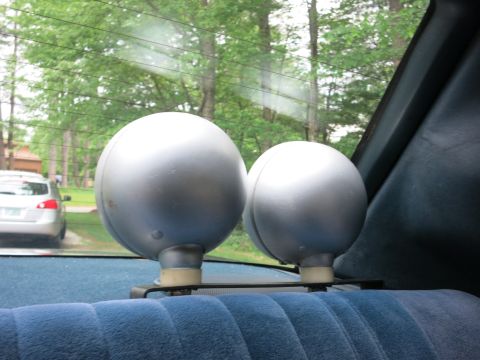 1991 Ford LTD Crown Victoria - Two large silver spherical lights mounted on a car's rear parcel shelf, seen through the back window with trees outside.