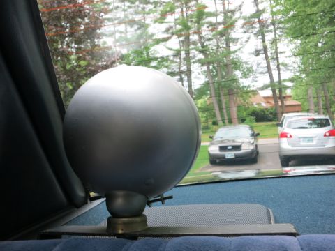 1991 Ford LTD Crown Victoria - single silver spherical light on a car's rear parcel shelf, with parked cars and a house visible through the rear window.