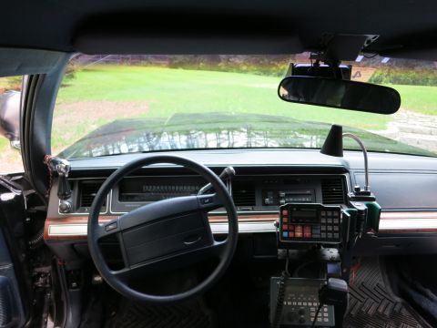 1991 Ford LTD Crown Victoria - Driver-side dashboard and steering wheel of a car fitted with a mounted two-way radio and microphone control head.