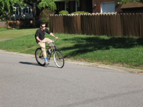 1994 Ford Bronco - A man pedals a motorized bicycle down a paved road, with a wooden fence and houses in the background.