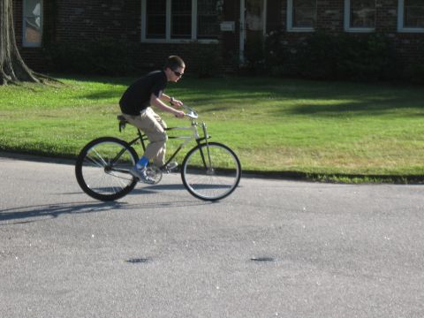 1994 Ford Bronco - A person rides a bicycle on a paved road in front of a brick building and a grassy lawn.
