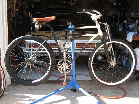 1994 Ford Bronco - A custom cruiser bicycle is mounted on a repair stand in a garage, with a vintage car visible in the background.