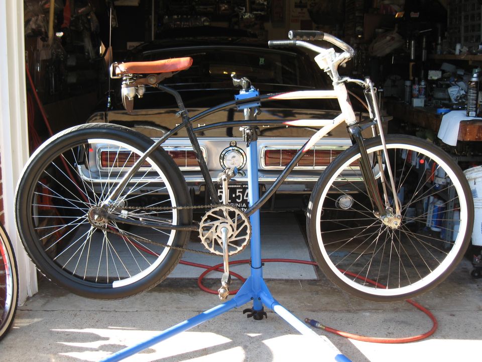 Custom cruiser bike on stand in front of a classic car