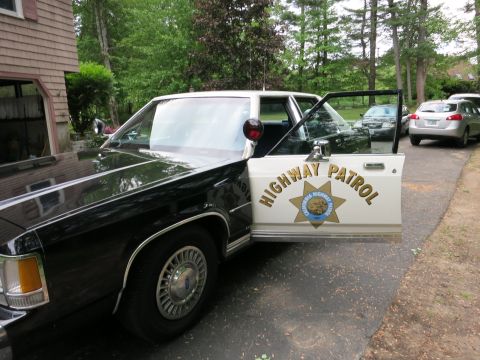 1991 Ford LTD Crown Victoria - black-and-white sedan with an open door reading HIGHWAY PATROL in gold lettering beside a star-shield badge in a driveway.