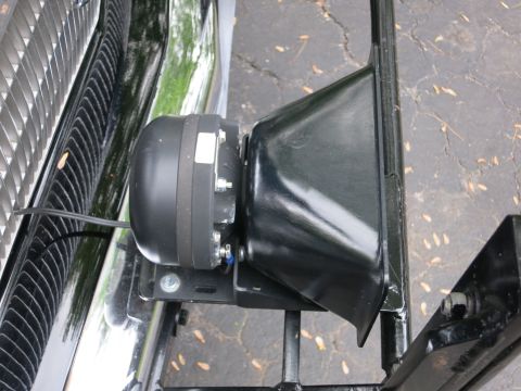 1991 Ford LTD Crown Victoria - black public-address speaker mounted on a metal bracket behind a vehicle's grille, viewed over pavement.