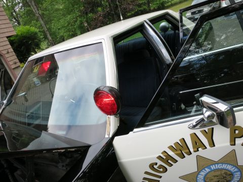 1991 Ford LTD Crown Victoria - Close-up of a black-and-white police car's open door showing a red emergency light and a California Highway Patrol star decal.