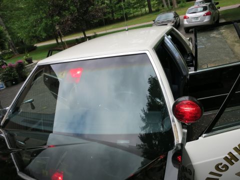 1991 Ford LTD Crown Victoria - Overhead view of a black-and-white police sedan's white roof and windshield with red interior lights, parked outdoors.