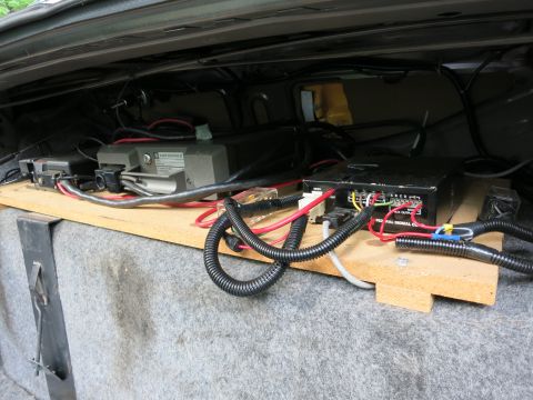 1991 Ford LTD Crown Victoria - Close-up of trunk-mounted electronic boxes and a dense bundle of red, black and colored wiring on a wood board.