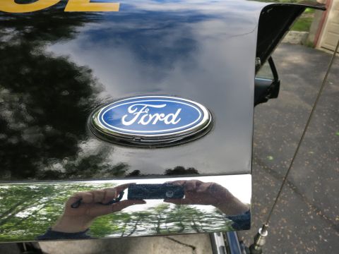 1991 Ford LTD Crown Victoria - Blue oval Ford emblem on a glossy black trunk lid, with the photographer reflected in the chrome trim below.
