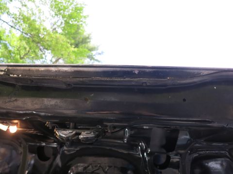 1991 Ford LTD Crown Victoria - Close-up of the rear sheet metal and bumper of a glossy black car body shot from below against a bright sky.