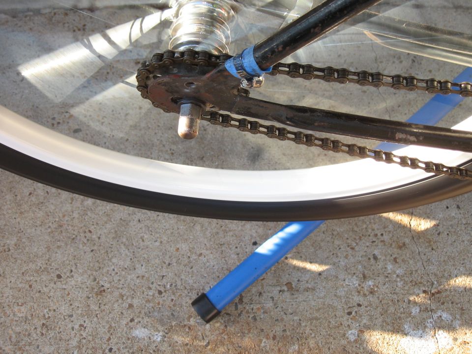 Close-up of bicycle chain, sprocket, and white-rimmed wheel on a stand