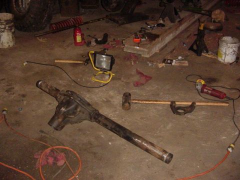 1992 Ford Bronco - A vehicle axle and various tools are laid out on a concrete floor, suggesting a repair or modification project is underway.