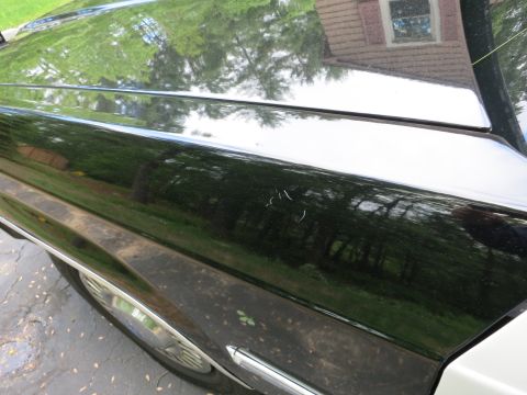 1991 Ford LTD Crown Victoria - Glossy black car rear quarter panel and trunk edge reflecting trees, sky and a brick house in the paint.