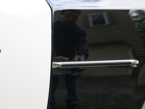 1991 Ford LTD Crown Victoria - Close-up of a chrome door handle on the glossy black lower door panel of a car, with a person's reflection visible in the paint.
