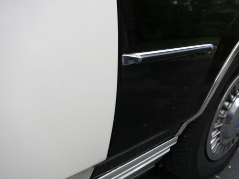 1991 Ford LTD Crown Victoria - Two-tone black-over-white car body panel with chrome belt molding and a chrome wire-spoke wheel cover at right.