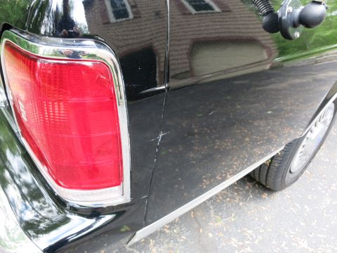 1991 Ford LTD Crown Victoria - Vertical red-and-chrome taillight on the black rear quarter panel of a car, with a chrome wire wheel and rocker trim visible.