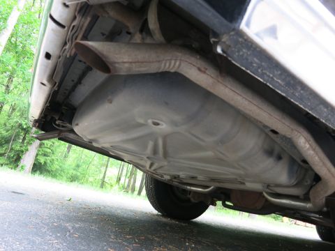 1991 Ford LTD Crown Victoria - Low-angle undercarriage shot showing the stamped floor pan, exhaust pipe and rear tire of a vehicle on pavement.