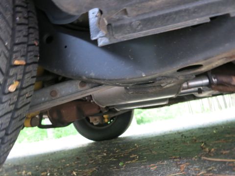 1991 Ford LTD Crown Victoria - Undercarriage view of a vehicle's rear suspension, axle, exhaust components and tire over a paved surface.