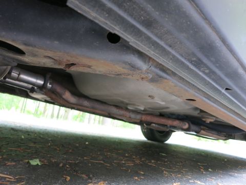 1991 Ford LTD Crown Victoria - Undercarriage view showing a surface-rusted exhaust pipe and frame rail beneath the rocker panel of a vehicle.