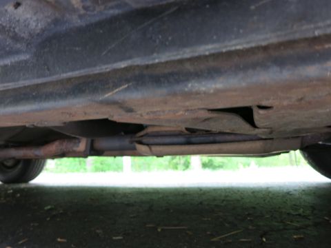 1991 Ford LTD Crown Victoria - Underside view along a vehicle's rocker and floor showing an exhaust pipe and patches of surface rust.