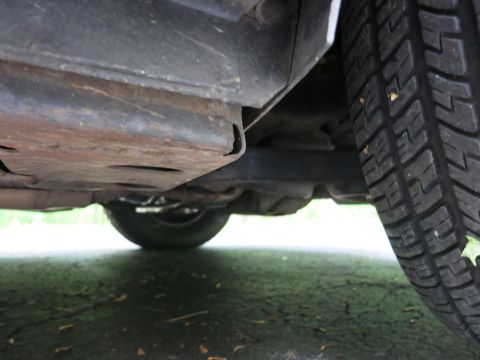 1991 Ford LTD Crown Victoria - Undercarriage view near a rear tire showing a rusty floor pan, exhaust line and the deep-tread tire sidewall.