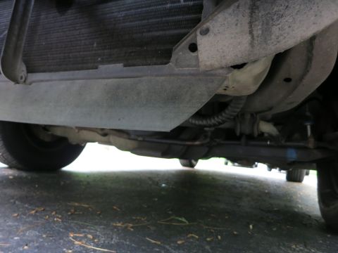 1991 Ford LTD Crown Victoria - Underside view of a vehicle's front radiator support, lower skid pan and routed wiring over pavement.