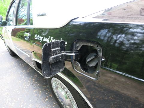1991 Ford LTD Crown Victoria - Open fuel-filler door and cap area on the black rear fender of a two-tone Grand Marquis with 'Safety and Service' lettering and a wire whee…