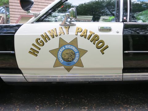 1991 Ford LTD Crown Victoria - Close-up of a black-and-white police car door showing the gold California Highway Patrol star emblem and 'Highway Patrol' lettering.