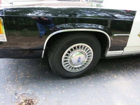 1991 Ford LTD Crown Victoria - Rear quarter and wheel of a glossy black police car fitted with a Ford-logo chrome wheel cover on a wide tire.