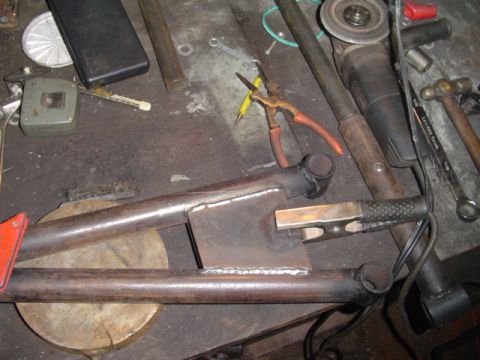 1993 Ford Bronco - A shop-welded steel A-frame or Y-shaped weldment of round tube joined to a flat gusset plate, laid out on a workbench with fresh weld beads…
