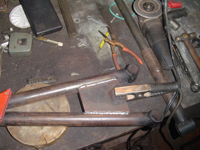 Welded steel tube weldment with gusset plate on a workbench beside grinder, hammer and pliers