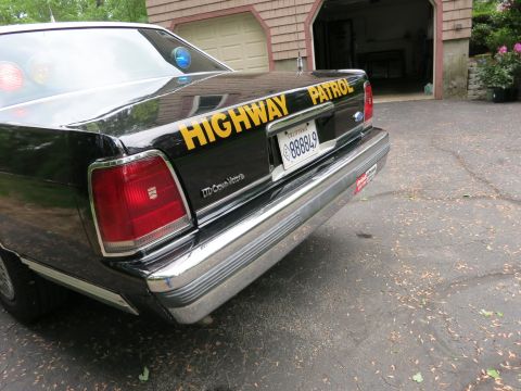 1991 Ford LTD Crown Victoria - Low-angle rear corner of a black Ford LTD Crown Victoria police car with 'Highway Patrol' lettering and a California license plate.