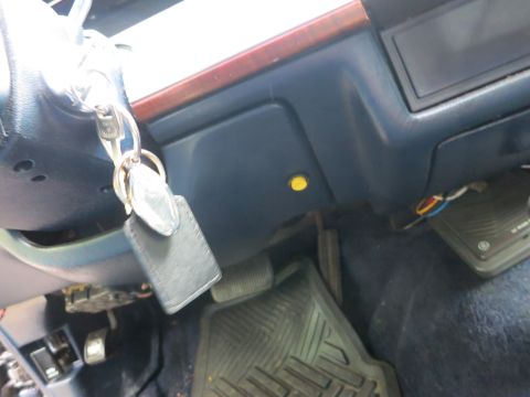 1991 Ford LTD Crown Victoria - Car keys on a leather fob hang from the steering column above a blue lower dash, pedals and rubber floor mat.