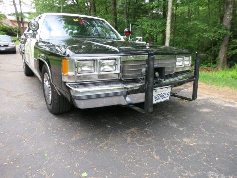 1991 Ford LTD Crown Victoria - Front three-quarter view of a black-and-white police car with quad headlights, a steel push bar, spotlights and a California plate.