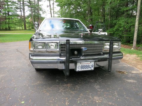 1991 Ford LTD Crown Victoria - Head-on front view of a black Ford police sedan with quad headlights, Ford grille badge, steel push bar and California license plate.
