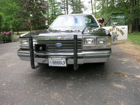 1991 Ford LTD Crown Victoria - Front of a black police car with a Ford grille badge and steel push bar; an open white door shows the CHP star and 'Highway Patrol'.