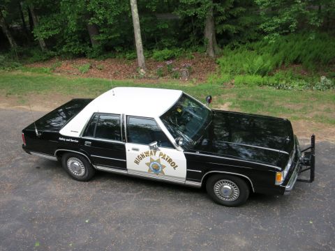 1991 Ford LTD Crown Victoria - High-angle full side view of a black-and-white California Highway Patrol police sedan with star door emblem and push bar on pavement.