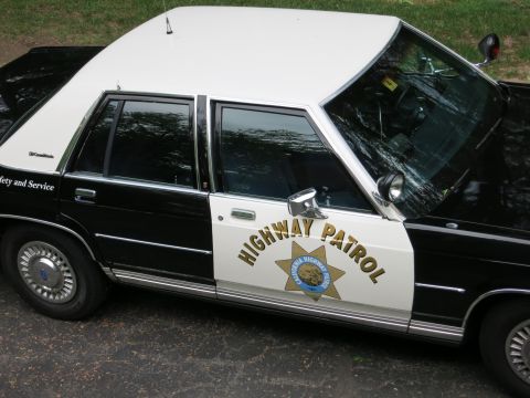 1991 Ford LTD Crown Victoria - Side view of a black-and-white CHP police sedan with the gold California Highway Patrol star emblem and 'Highway Patrol' on the door.
