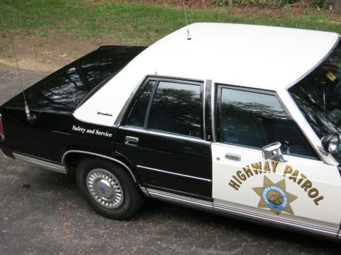 1991 Ford LTD Crown Victoria - High-angle rear-side view of a black-and-white CHP police sedan with 'Safety and Service' lettering and the gold star door emblem.