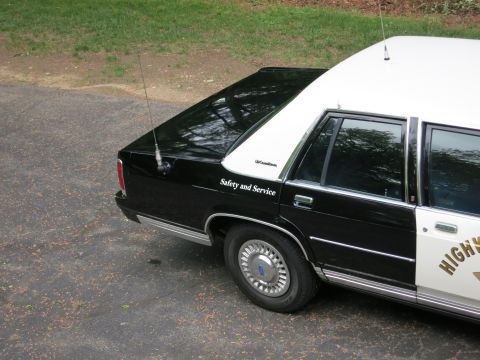 1991 Ford LTD Crown Victoria - Rear-quarter view of a black-and-white CHP police sedan reading 'Safety and Service' with a Ford-badged wheel cover and roof antenna.