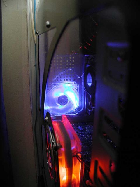 1993 Ford Taurus - Dark interior shot of a computer case looking past the open side panel at a blue-LED clear case fan and an orange-lit fan below it, with th…