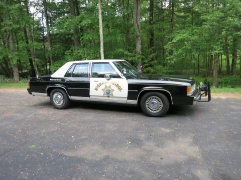 1991 Ford LTD Crown Victoria - Front three-quarter view of a black-and-white police cruiser marked Highway Patrol with a front push bumper, parked beside woods.