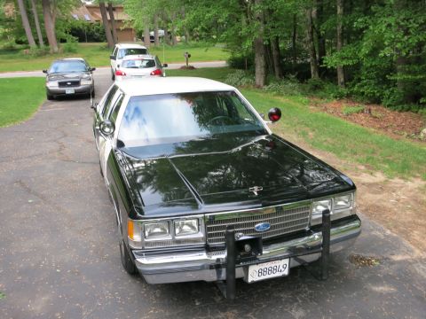 1991 Ford LTD Crown Victoria - Elevated front view of a black Ford sedan with chrome grille and push bumper, parked in a driveway with other vehicles behind it.