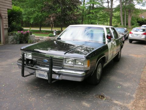 1991 Ford LTD Crown Victoria - Front three-quarter view of a black-and-white Ford sedan with a chrome push bumper and California plate 888849, parked beside a house.
