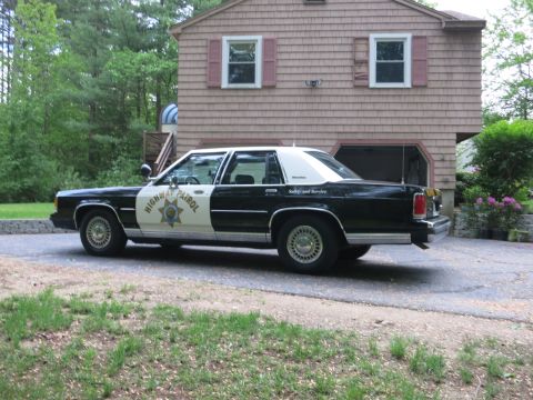 1991 Ford LTD Crown Victoria - Driver-side rear three-quarter view of a black-and-white Highway Patrol cruiser parked on a driveway beside a shingled house.