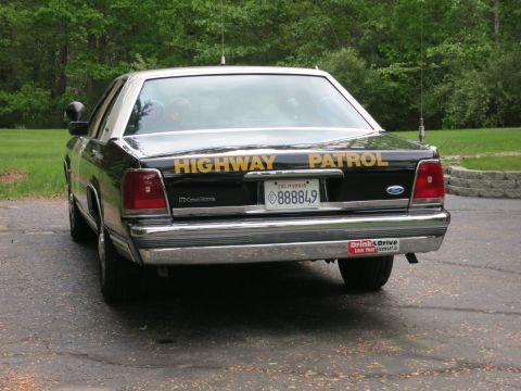 1991 Ford LTD Crown Victoria - Rear view of a black Ford Crown Victoria police cruiser with yellow Highway Patrol lettering and a California license plate reading 888849.