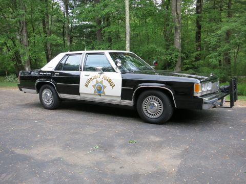 1991 Ford LTD Crown Victoria - Front-right view of a black-and-white Highway Patrol police sedan with a chrome grille, push bar, and gold star door emblem on a paved lot.