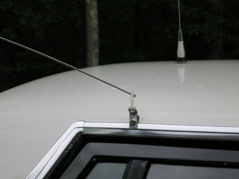 1991 Ford LTD Crown Victoria - Close-up of a thin whip antenna and a short stubby antenna mounted on the white roof of a car near the window trim.