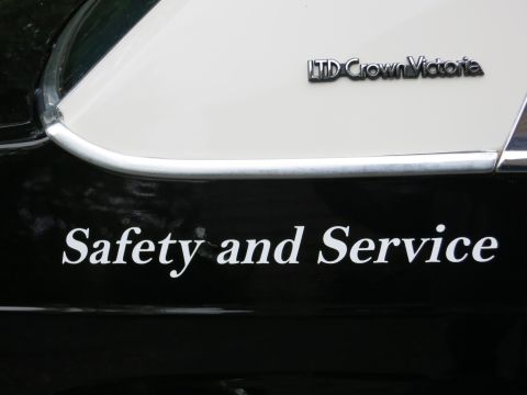1991 Ford LTD Crown Victoria - Close-up of a chrome 'LTD Crown Victoria' emblem on white bodywork above white 'Safety and Service' lettering on a black door.
