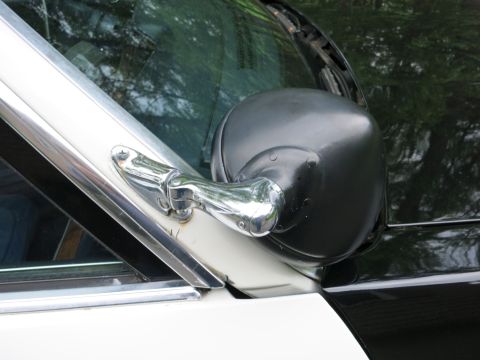 1991 Ford LTD Crown Victoria - Close-up of a black exterior side mirror on a chrome mounting arm attached to the A-pillar of a white-and-black car.